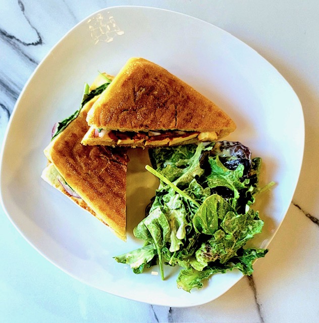 A sandwich and a salad on a white plate on a marble counter 