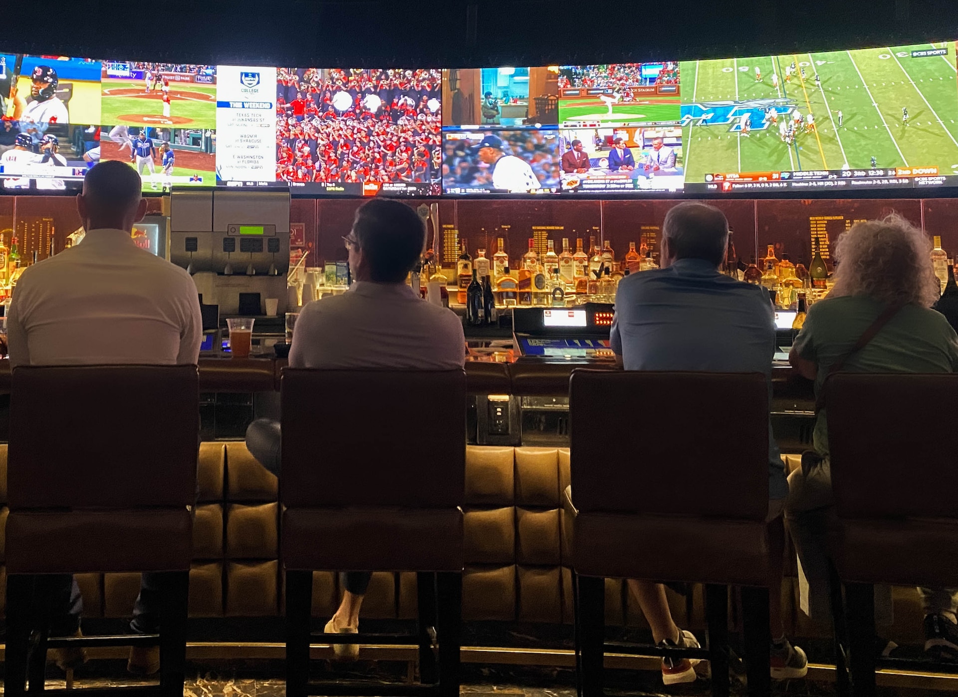 A group of people sitting at a bar watching sports games on tv.