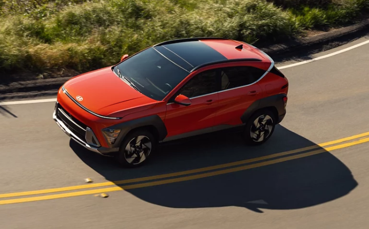 Orange paint color 2024 Hyundai Kona driving down highway on sunny day in Dublin, CA.