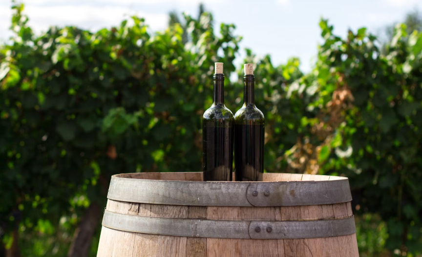 Two wine bottles sitting on a wood barrel in a Livermore, CA winery and vineyard.