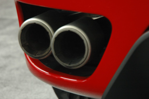 Red painted car close up on tailpipe emitting exhaust smoke.